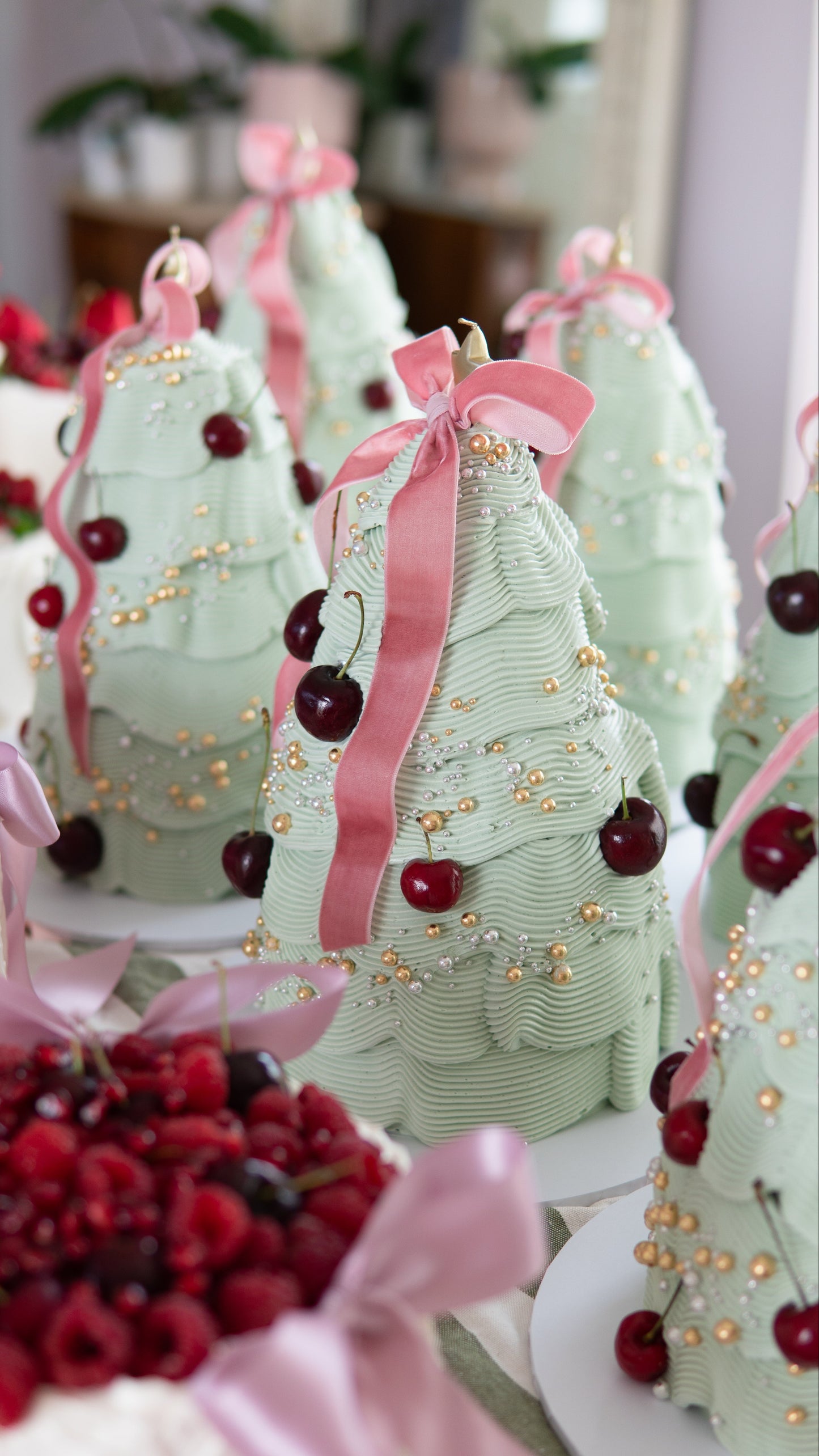 Decorative Christmas trees cake with pink ribbons and cherries on a white surface.